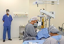 Surgeon operating using microscope while theatre staff attend