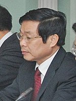 Nguyễn Bắc Son presumably sitting and looking leftwards. Wearing glasses, a grey suit, a red tie and a white shirt.