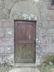 A wooden door on a granite wall. The top of the door is iniscribed "ES YGLESIA DE REFUGIO".