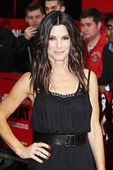 A portrait of Sandra Bullock wearing a black dress, with paparazzi standing in the background.