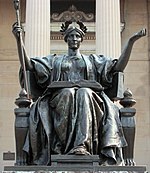 Bronze statue of a crowned woman sitting with an open book on her lap