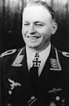 A smiling man wearing a military uniform and an Iron Cross displayed at the front of his uniform collar.