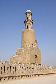 Photo of a minaret in four levels, with battlements in the foreground