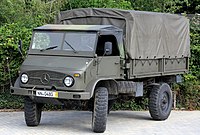 A military Unimog S 404 truck painted in camouflage in front of a forest background.