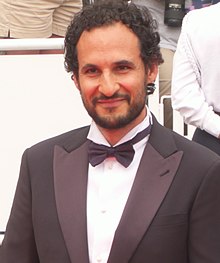 Ali Abbasi, wearing a dark suit with bowtie and a white shirt, smiling and looking just right of camera
