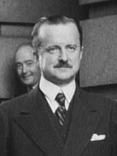 head and shoulders photograph of man in lounge suit, with dark, slicked back hair and a small moustache