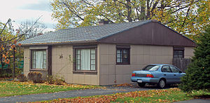A brown house with the same grid-pattern siding and a blue car parked in a driveway on the left.