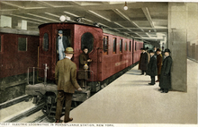 An electric locomotive at a station platform with men waiting to board