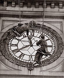 Photograph of two cleaners working on the clock face.