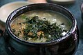 Gamja-ongsimi topped with gim-garu (seaweed flakes) and toasted sesame seeds, served in ttukbaegi (earthenware)