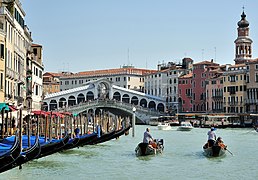 Two gondoliers pull out with clients on board from a row of gondolas on the Grand Canal near the Rialto Bridge