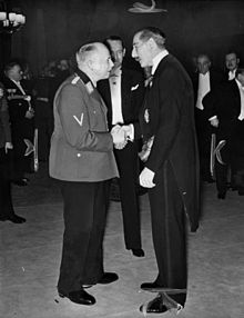 Two men shake hands surrounded by other men in formal dress