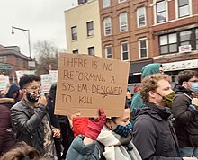 Demonstrators march in the street. One person holds as sign with the words, "There is no reforming a system designed to kill".