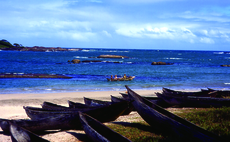 a dozen black wooden canoes on the sand of a vast bay