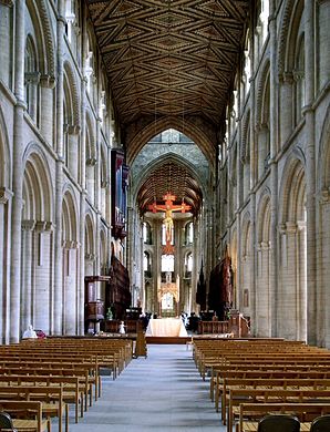 The nave of Peterborough Cathedral (1118–1193) in three stages of arcade, gallery & clerestory, typical of Norman abbey churches. The rare wooden ceiling retains its original decoration (c. 1230). Gothic arches beneath tower (c. 1350).