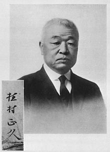 An older Japanese man wearing a dark western suit and tie
