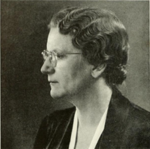 A woman with short hair and glasses, facing right of camera
