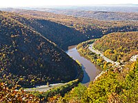 Aerial view of a river turning between rolling hills with forests in fall colors