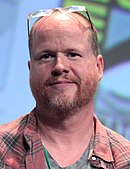 Informal bust-length colour photograph of Joss Whedon, spectacles raised over forehead, bearded, smiling, in checked jacket
