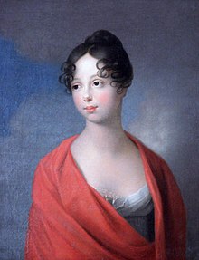 Young woman in a simple white empire dress with a low neckline and a red cape on her shoulders. She is looking into the distance before the backdrop of the sky. Her hair is black in an updo with curls and her eyes are dark. Her skin is very light white, with blush on her cheeks.