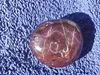 A pink-colored gem with an irregular shape set on a purple background.