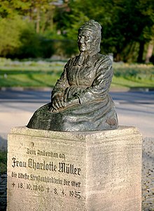 Bronzeskulptur einer sitzenden Alten Frau. Auf dem Sockel steht: "Dem Andenken an Frau Charlotte Müller, die älteste Straßenhändlerin der Welt. Geb. 18.10.1840, gest. 08.04.1935"
