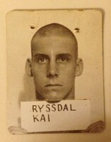 Sepia portrait of a man with a buzzcut holding up a card that says "RYSSDAL, KAI" on it