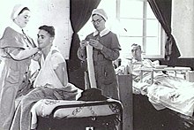 Black and white photo of two men in hospital beds with two female nurses standing next to one of the men