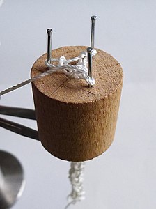 three nails driven into a drilled-out dowel, with knitting being made on them