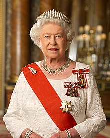 Queen Elizabeth in the Blue Room of Buckingham Palace. She is wearing: a diamond fern brooch, Queen Mary's Fringe Tiara, the City of London Fringe Necklace, the insignia of the Sovereign of the Order of New Zealand, the badge of the Queen's Service Order, and the sash and star of the New Zealand Order of Merit.