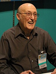 An bald elderly man in a brown shirt.