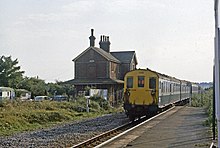 A diesel train with an old station building in the background