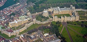 An aerial photograph of Windsor Castle, with three walled areas clearly visible, stretching left to right. Straight roads stretch away in the bottom right of the photograph, and a built-up urban area can be seen outside the castle on the left.