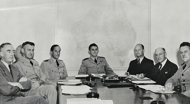Four men in military uniforms and three in civilian clothes seated at a table