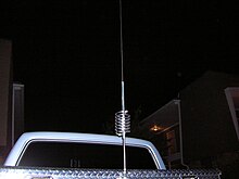A tall antenna with a helical coil in the middle, mounted on pickup-truck metal tool box
