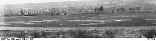 A black and white photograph of a landscape with a railway embankment in the middle distance, behind which is a village