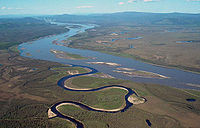 Aerial photo of the narrow horseshoe-bent Charley River flowing into the wide Yukon river with islands in the middle and nearby lakes