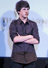 A teenage boy is standing up, with his arms crossed.