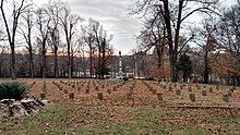 A late fall view of a cemetery. The headstones are in rows, and a statue of a soldier and a flag are in the background