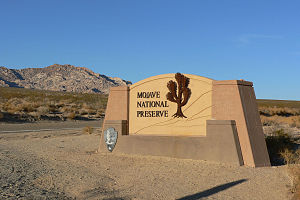 Sandstone-colored welcome sign with "Mojave National Preserve", the NPS logo, and a tree
