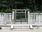 Wooden torii gate behind a stone fence in front of trees.