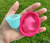 A menstrual disc and mentrual bell are held next to each other. The disc is larger in diameter and flatter. It has a similarly thick rim and thinner material in the basin.