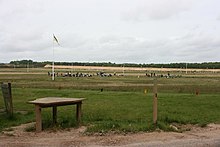 Photograph of a shooting range, with yellow-and-blue wind flags visible.