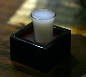 Nigori is an unfiltered sake, presented here in an overflowing glass within a traditional wooden box cup, symbolizing abundance.
