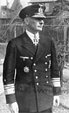 A man wearing a military uniform and peaked cap with a military order in shape of a cross displayed at the front of his uniform collar.