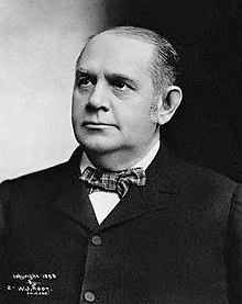 A black-and-white head-and-shoulders photograph of a respectfully turned-out middle-aged gentleman in a tartan-pattern bow-tie, white shirt and dark jacket