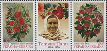 Drei Briefmarken sind nebeneinander angereiht. Die beiden Äußeren zeigen gemalte rote Blumensträuße, das Mittlere zeigt eine Frau mit slawischer Kopfbedeckung und bunte Blumen über ihrem Kopf.