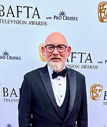 Tim Reid, wearing a black tuxedo suit in front of the BAFTA backdrop