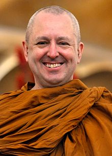 Caucasian Buddhist monk wearing saffron robes, grinning at camera