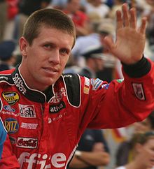 Edwards, with close cropped hair, waves while wearing his red, sponsor-filled racing suit.